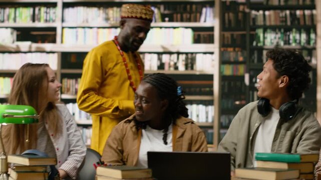 Diverse classmates in group study gather around laptop with study materials at library table, study desk with books, sharing ideas during collaborative learning session, for online learning.
