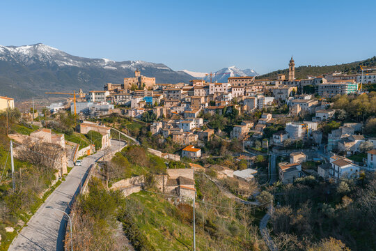 Aerial view of the historic town of Capestrano featuring stone buildings, a prominent castle, and a church bell tower nestled against snow-capped mountains in Capestrano, Abruzzo, Italy.