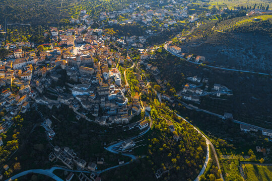 Aerial view of the historic hilltop town of Capestrano with its dense stone buildings, winding roads, and surrounding lush green hillsides in Capestrano, Abruzzo, Italy.