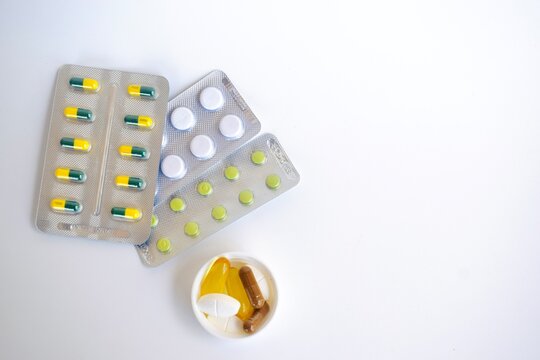Flat lay composition of various medical blister packs and a plastic bottle cap filled with colorful supplement capsules and tablets.