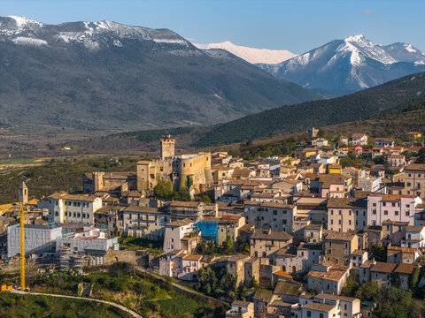 Aerial view of Castello Piccolomini overlooking the historic stone buildings of Capestrano with snow-capped mountains in the background in Capestrano, Abruzzo, Italy.