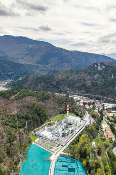 Aerial view of the Edison power plant with its tall striped chimney, industrial facilities, and surrounding forested hills in Bussi Officine, Abruzzo, Italy.