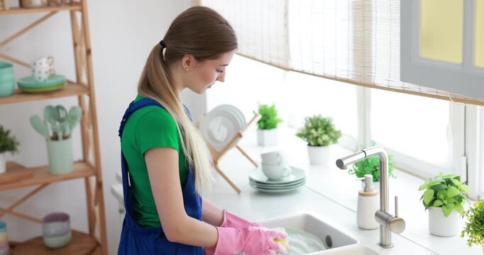 Teenage worker washing dishes near sink in kitchen. Part-time job