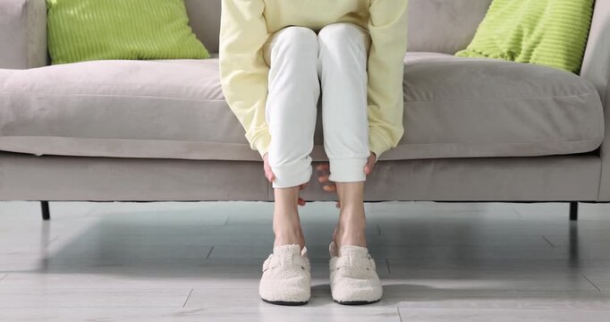 Woman suffering from leg pain on sofa at home, closeup