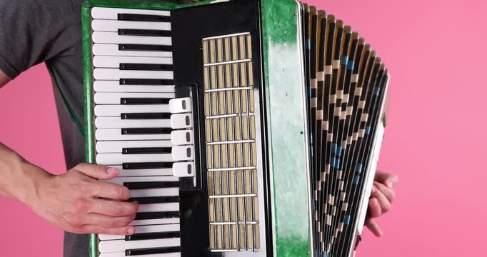 Man playing piano accordion on pink background, closeup