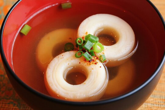 Japanese Osuimono clear soup with maki-fu wheat gluten circles and vegetables in a red rimmed bowl. Food is garnished with green onions and chili flakes. Warm, healthy dish for lunch.