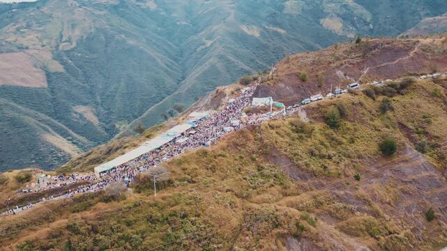 Aerial drone orbit view of thousands of catholic pilgrims gathering at a mountain crossroads shortcut during the Virgen del Cisne procession in Loja, Ecuador.