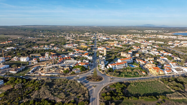 Aerial view of the town of Sagres featuring a central roundabout, white buildings with red roofs, and surrounding coastal landscape under a clear blue sky in Sagres, Faro, Portugal.