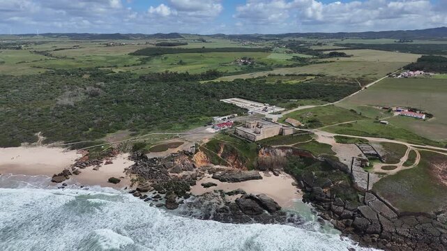 Aerial view panning left over the rugged coastline and the historic fortress Forte da Praia do Pessegueiro near Porto Covo, Portugal, along the scenic Fisherman's Trail and Rota Vicentina.