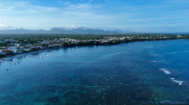 Aerial view of the coastline of Mauritius Island with turquoise waters, small boats, and buildings along the shore in Triolet, Pamplemousses District, Mauritius.