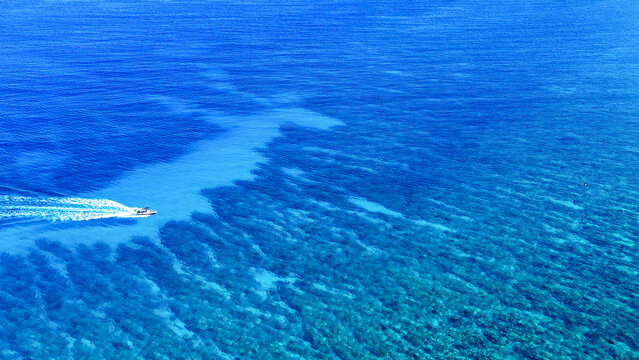 Aerial view of a motorboat leaving a white wake across the vibrant turquoise waters of the coral reef surrounding Mauritius Island in Triolet, Pamplemousses District, Mauritius.