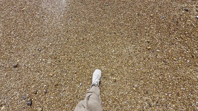 Male stepping along sandy coastal shore aerial