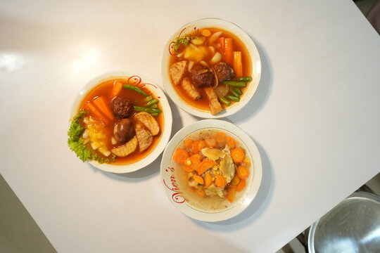  Top view of three Indonesian soup dishes with vegetables and selat solo, served on a white table in a casual dining setting.