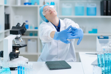 Fototapeta premium female lab scientist stretch hand exhausted feeling stress tired from working overtime in laboratory, asian technician relax despair overwhelmed intensive research experiment chemical liquid substance