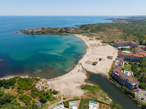 Aerial view of Nestinarka beach with its sandy shore, rows of umbrellas, surrounding hotels, and a river flowing into the Black Sea in Burgas, Bulgaria.