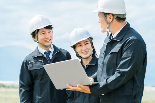 建設現場でノートパソコンを見ながら打ち合わせをする作業着姿の男女の作業員