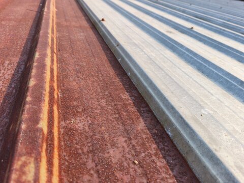 Close up of rusted corrugated metal roof sheets with weathered texture, high angle view of an old brown rusty iron canopy panel damaged by water and oxidation needing house renovation