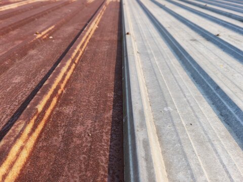 Close up of rusted corrugated metal roof sheets with weathered texture, high angle view of an old brown rusty iron canopy panel damaged by water and oxidation needing house renovation