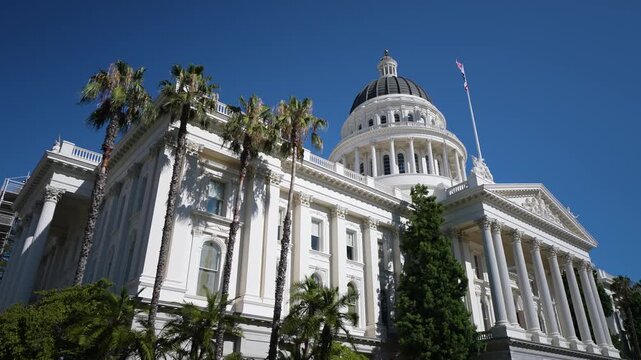 Sight of California State Capitol in Sacramento on sunny day with bright sky and green palm trees by the building