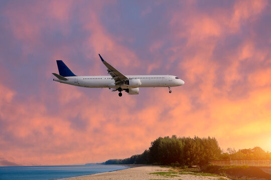 White passenger airplane with landing gear deployed flies low over a tropical sandy beach and calm ocean