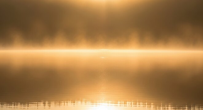 Golden sunrise haze shimmering over tranquil water surface