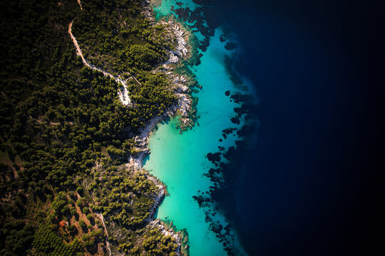 Aerial view of the Sithonia peninsula coastline with turquoise waters, rocky shores, and dense pine forests in Halkidiki, Greece.