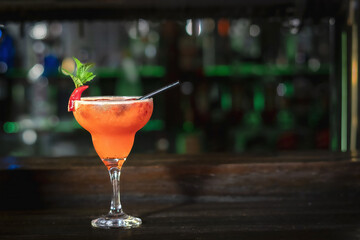 Refreshing red cocktail in a glass garnished with a red chili pepper and fresh mint leaf on a rustic bar counter with beautiful bokeh lights background. © Rodrigo Farias