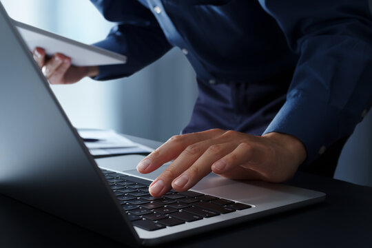 Businessman using laptop computer at desk and looking at digital tablet. Closeup of hands and keyboard. Business technology concept.