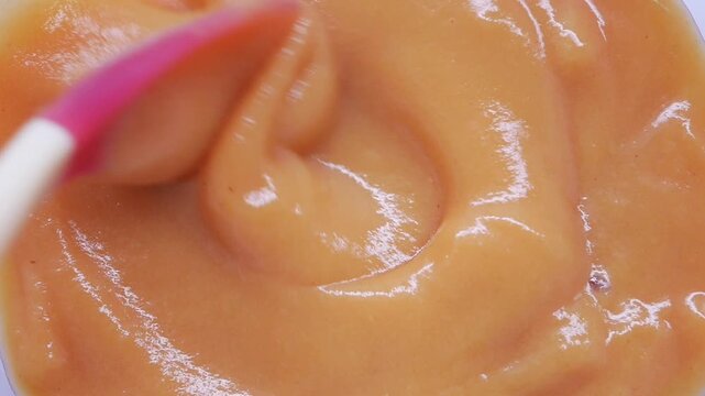Mixing baby food in a bowl with a pink spatula