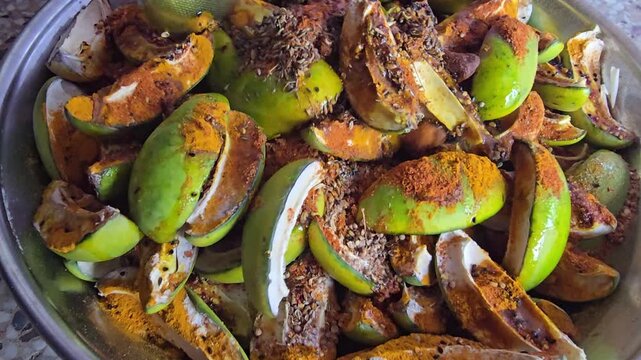 Spiced green mango slices for traditional pickle making, raw mango pieces coated in turmeric and chili powder, organic fruit preservation process