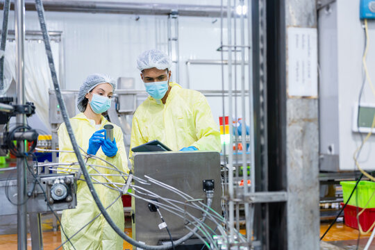 Quality control inspectors examining tin can on production line in food factory, Technical team checking manufacturing machinery, Industrial quality assurance team monitoring production process