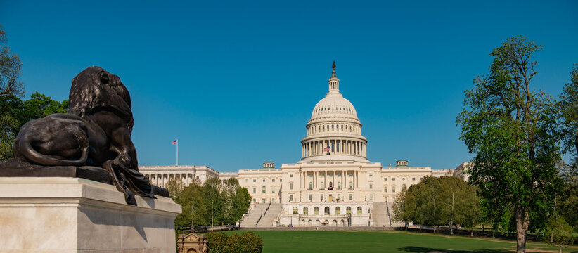Capitol building under blue sky. American Capitol with waving flag. Capitol dome above Congress facade. Historic Capitol in Washington DC.