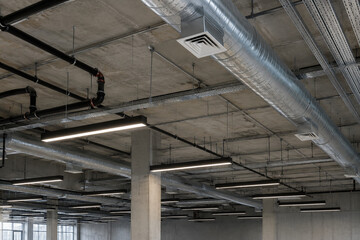 Naklejka premium Industrial ceiling with exposed ductwork, pipes, and lighting fixtures in a modern building under construction or renovation.
