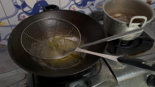 Close up of frying tool mesh strainer over hot oil stall preparation