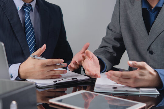 Close up of business professionals gesturing during a corporate meeting with financial documents and a tablet, depicting team collaboration, strategic planning, and professional advisory services.