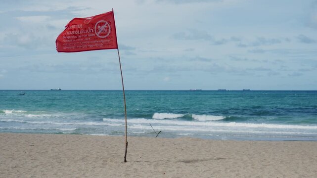 4K  Slow motion red warning flag on sandy beach with blurry sea background