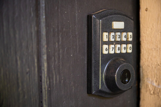 Close-up of a black keypad door lock mounted on a dark wooden door, showing number buttons, keyhole, and modern home security hardware.