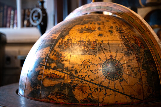Close-up of an antique decorative globe featuring an old world map with books and study decor softly blurred in the background.