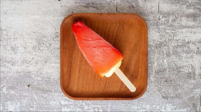 Timelapse: dissolution of fruit ice cream on wooden square plate, top view