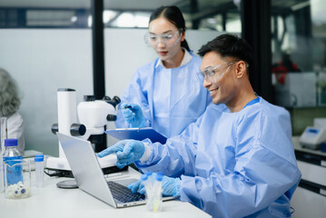 Two scientists collaborating in a modern biotechnology laboratory using laptop and microscope for...