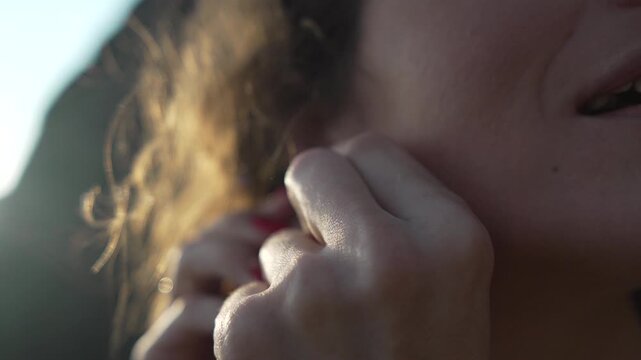 Woman putting jewelry. Close-up of a stylish woman adjusting a small earring on her earlobe during golden sunset light.