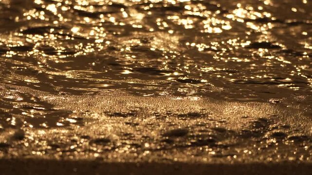Golden waves reflections wash, slow motion texture background reflecting warm sunset sunlight on beach sand