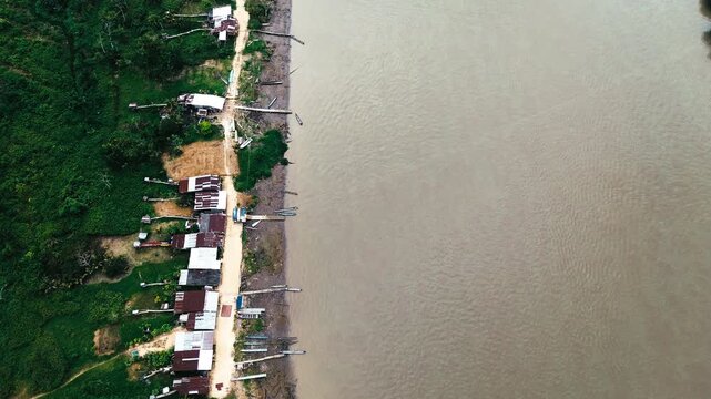 Top Down Drone View of Remote Amazon River Shore in Ecuador with Houses, Canoes, Brown Water and Tropical Forest Edge Landscape