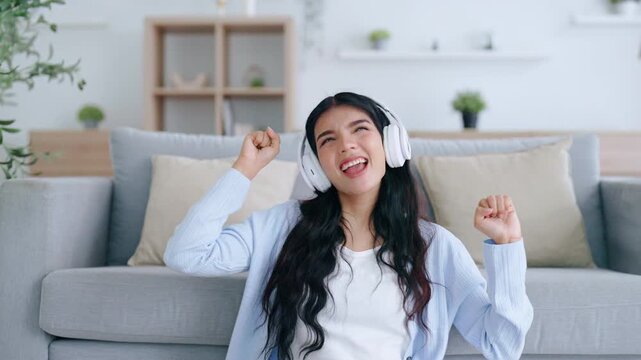 Young asian woman listening to music on couch in living room at home. Happy asia female wearing headset and sitting on the floor