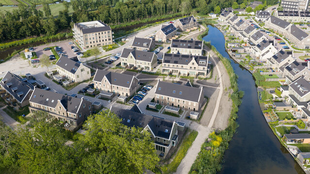 Purmerend, North Holland, Netherlands - 15 June 2026: Aerial view of a modern residential neighborhood featuring rows of houses with dark roofs, a winding canal, and lush green surroundings.