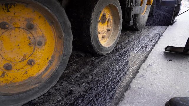 Asphalt Resurfacing Process and Roadworkers Tools Low Perspective. Ground-level shot showing three rows of asphalt paving machine wheels during hot tarmac laying. Road reconstruction.