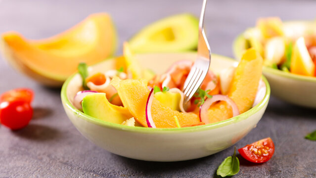 eating fresh melon salad with avocado prosciutto and onion using fork