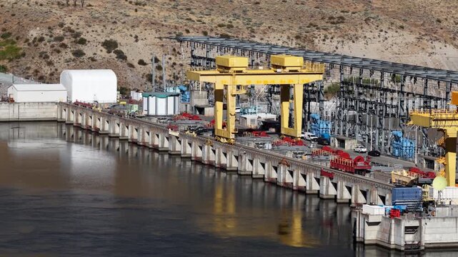 Aerial of industrial power facility along Columbia River near Azwell Washington with massive yellow gantry structures and concrete piers