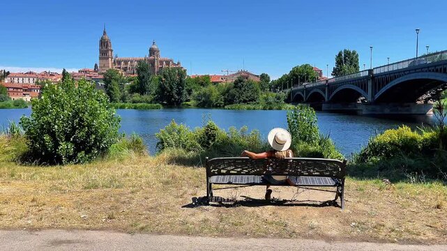 Woman on bench looking at Salamanca cathedral and river in Spain