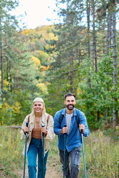 Hiking couple, young man and woman enjoys nature with trekking poles in a lush forest during a sunny day